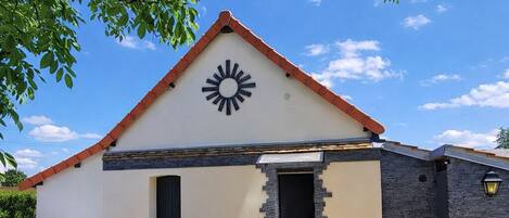 Una casa moderna con un motivo de sol en la fachada, una terraza de madera, mobiliario exterior y una estatua.