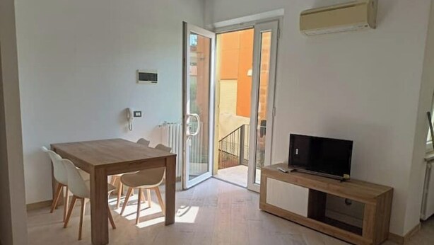 A modern apartment with a wooden dining table, a TV on a wooden stand, and a sliding glass door leading to a balcony. - Cozy ground-floor mini apartment a few meters from Rimini's dockyard (Rimini)