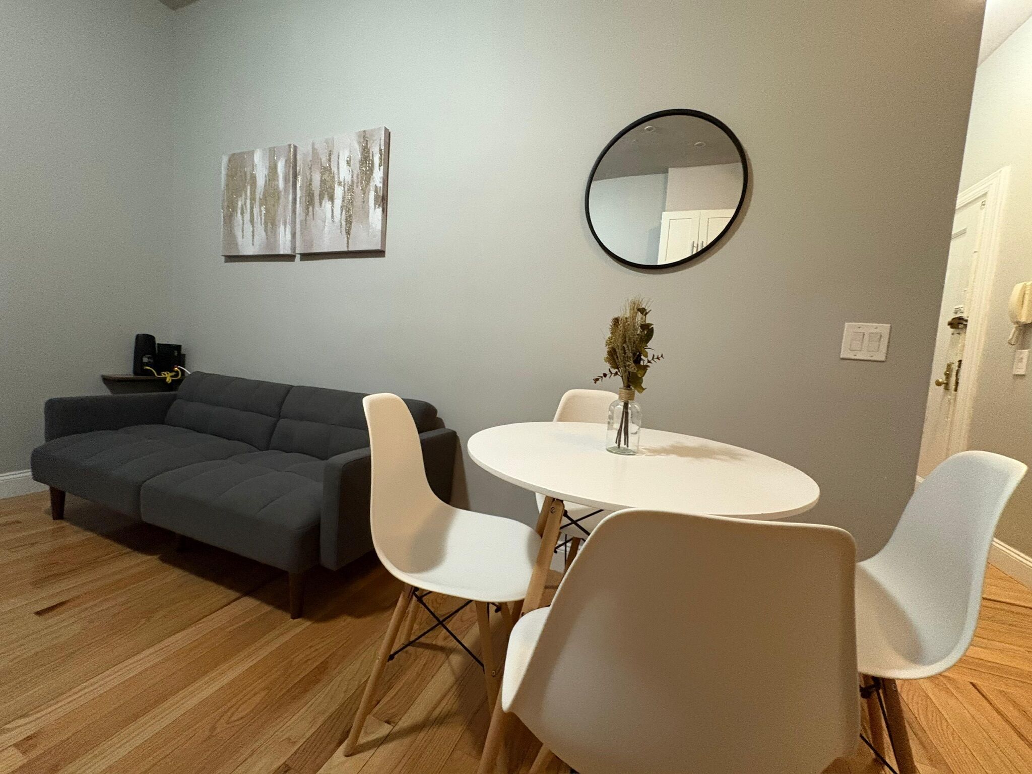A modern living room with a grey sofa, white chairs, a round table with a vase, and abstract wall art.