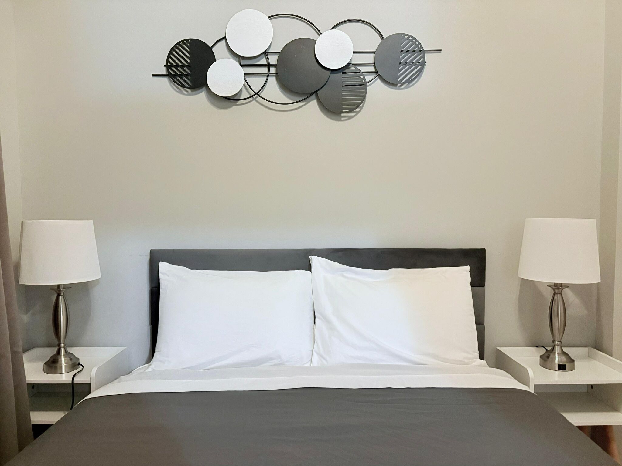 Una habitación de hotel moderna con una cama grande, dos mesitas de noche con lámparas y una obra de arte decorativa sobre la cama.