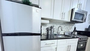 Une cuisine avec des armoires blanches, un réfrigérateur en acier inoxydable, un four à micro-ondes, une cuisinière et un évier.