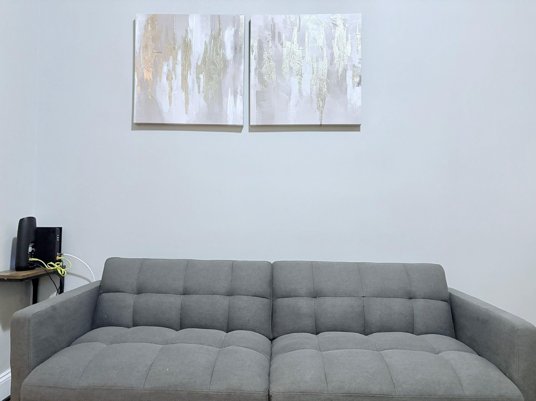 Ein graues Sofa in einem Raum mit zwei abstrakten Bildern an der Wand.