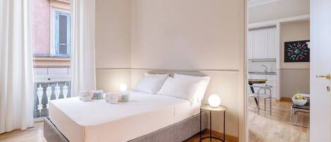 Un dormitorio con cama, mesitas de noche, ventana con cortinas y vistas al exterior.