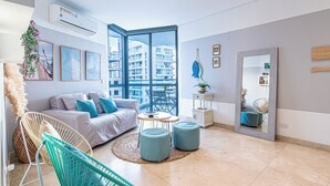 A modern living room with a sofa, two ottomans, a chair, a small table, and a large mirror. - Grand Marina Oceanview Apartments by Xarm Apartments (Santa Marta)