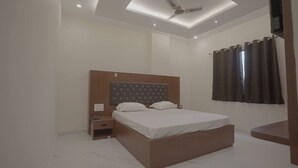 Quarto com cama, mesa de cabeceira, ventoinha no teto e janela com cortinas.