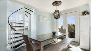 A dining area with a wooden table, wicker chairs, a chandelier, and a spiral staircase. - Crow's Nest at Blue Mountain Beach - Ocean View - Private Beach Access (Santa Rosa Beach)