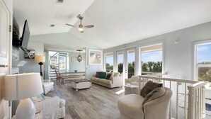 A spacious living room with a high ceiling, a ceiling fan, and large windows offering a view of palm trees. - Crow's Nest at Blue Mountain Beach - Ocean View - Private Beach Access (Santa Rosa Beach)