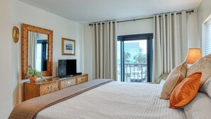 Une chambre d’hôtel avec un grand lit, une télévision, une commode, une fenêtre avec des rideaux et un balcon offrant une vue sur la ville.