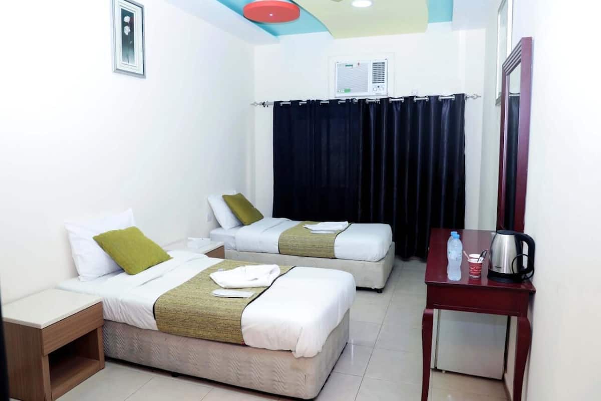 Une chambre d’hôtel avec deux lits, une petite table, une bouilloire, une bouteille d’eau et une tasse.