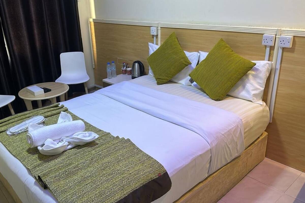 Une chambre d’hôtel avec un lit, deux chaises blanches, une petite table ronde et un plateau contenant des serviettes et une bouilloire.