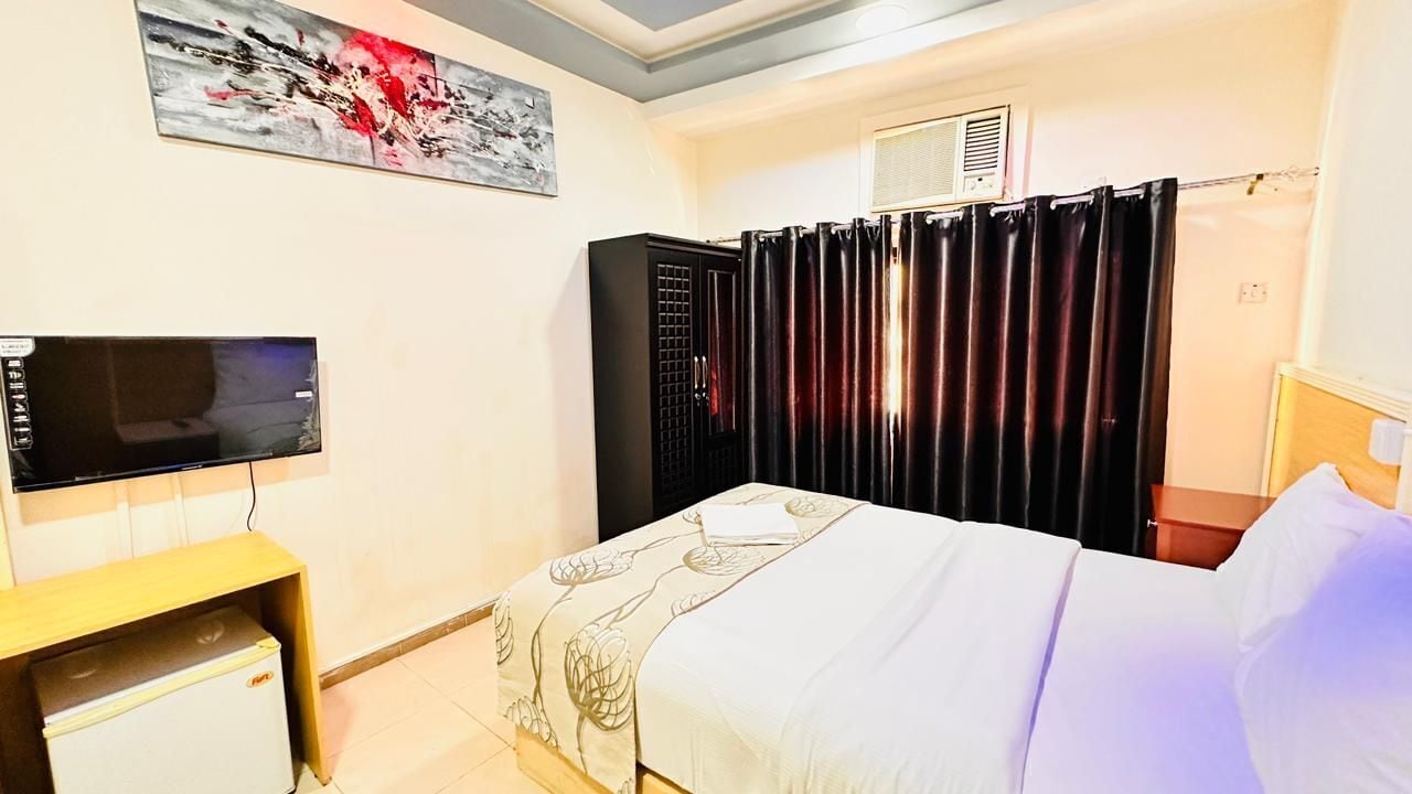 Habitación de hotel con cama, televisor, escritorio pequeño, calefactor, cortina y un cuadro en la pared.