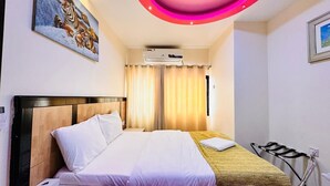 Ein Hotelzimmer mit Bett, Nachttisch, Wand-Klimaanlage und einem Fenster mit Vorhängen.