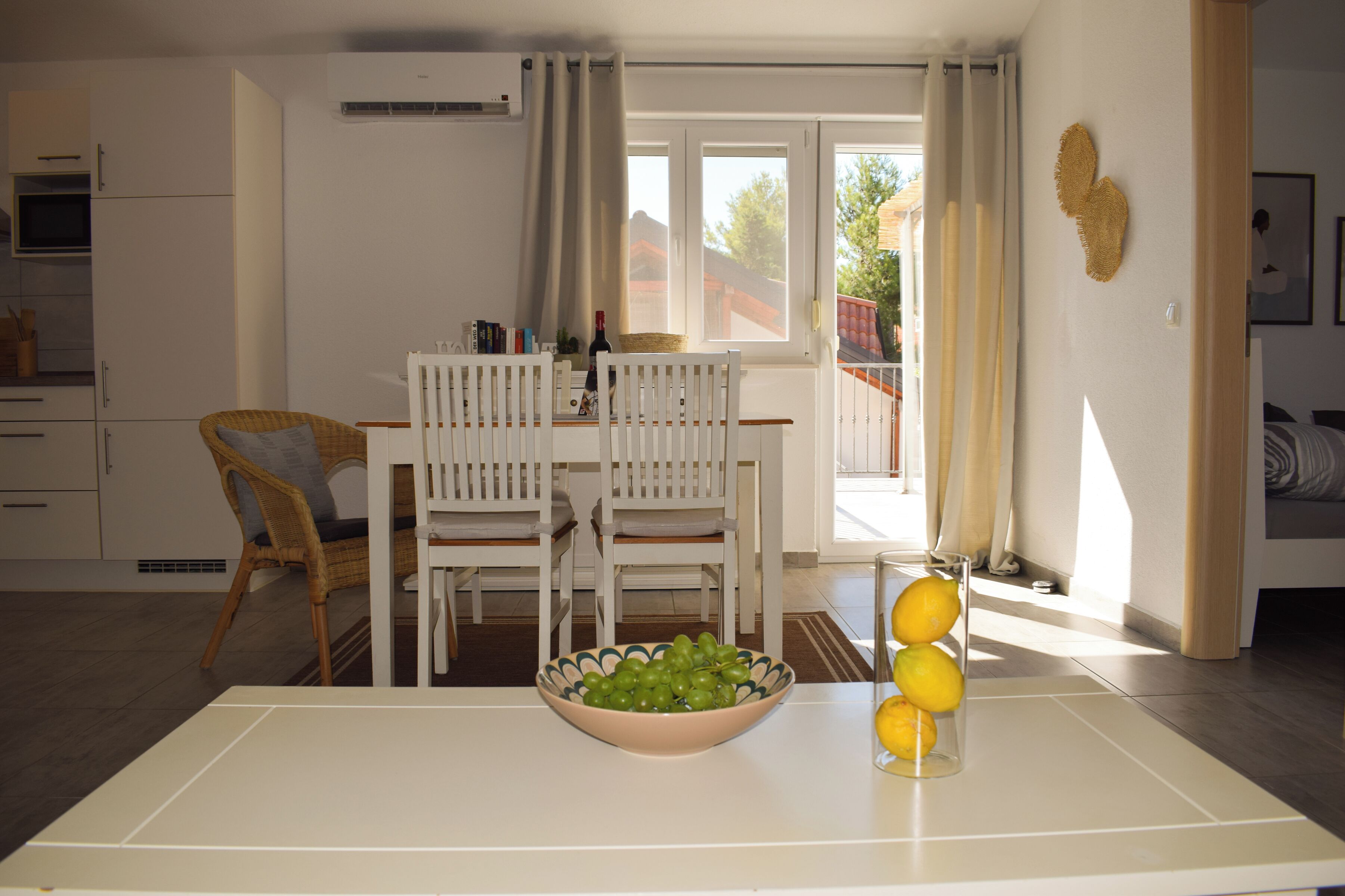 A dining area with a table, chairs, a bowl of fruit, and a window with curtains.