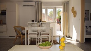 Een eetgedeelte met een tafel, stoelen, een schaal fruit en een raam met gordijnen.
