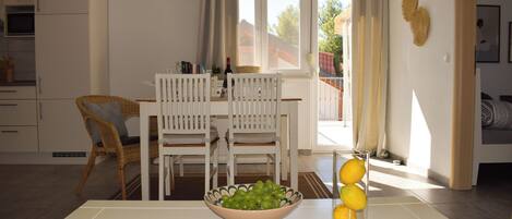 Ein Essbereich mit Tisch, Stühlen, einer Obstschale und einem Fenster mit Vorhängen.