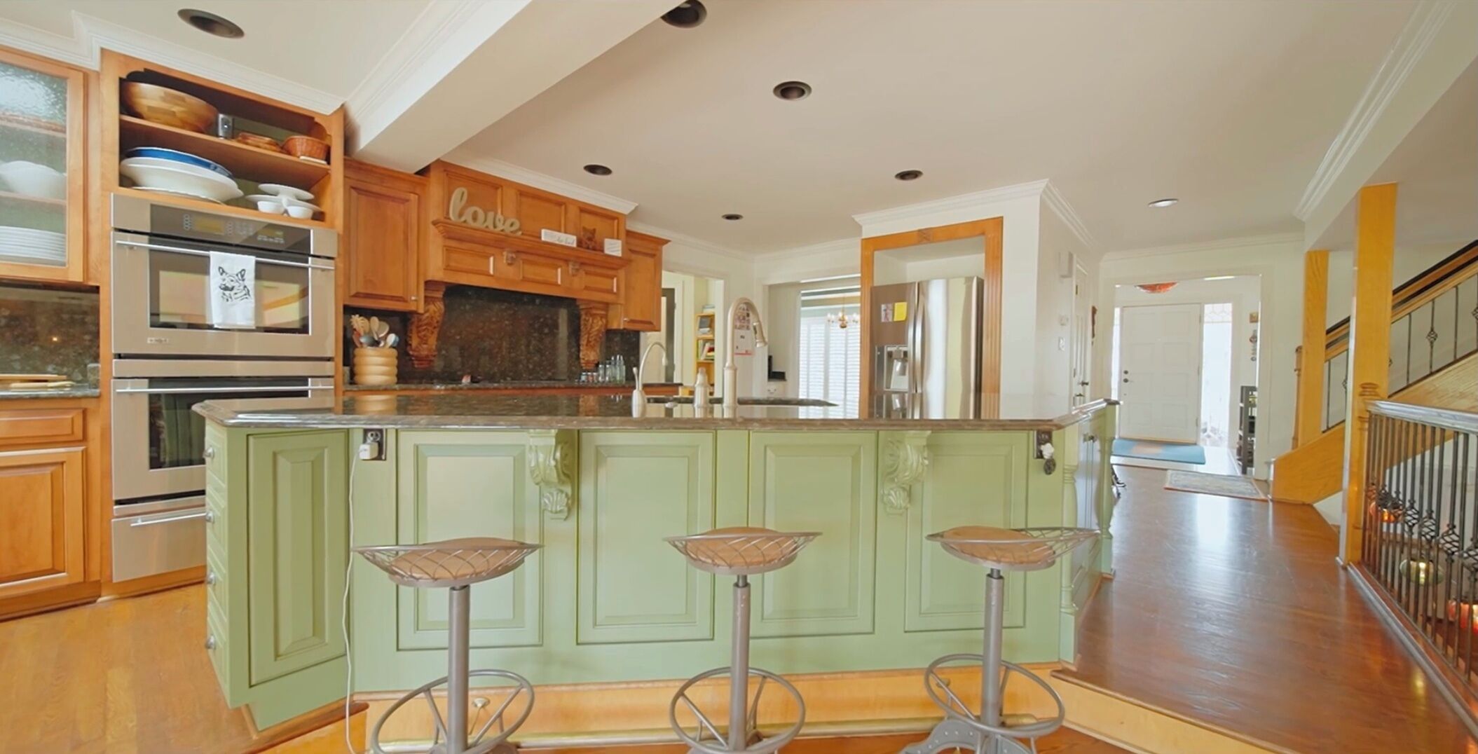 A spacious kitchen with a central island, wooden cabinets, and a "love" sign above the cabinets.