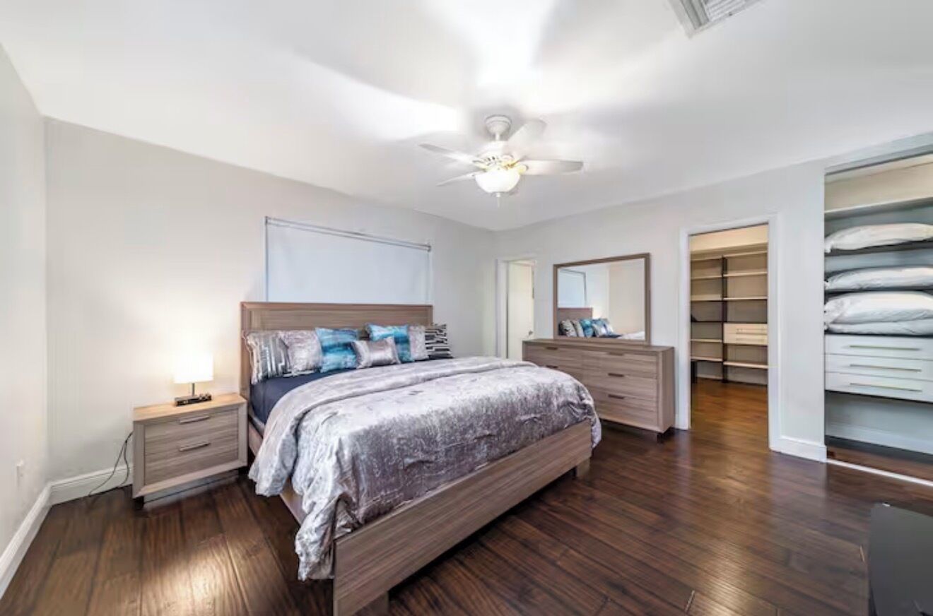 Une chambre à coucher comprenant un lit, des tables de chevet, une commode, un ventilateur de plafond et un dressing.