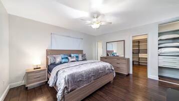 Une chambre à coucher comprenant un lit, des tables de chevet, une commode, un ventilateur de plafond et un dressing.
