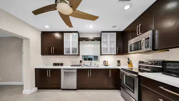 Una cocina moderna con gabinetes oscuros, electrodomésticos de acero inoxidable y un ventilador de techo.