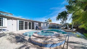 Un patio trasero con un jacuzzi, una piscina y un porche cubierto.
