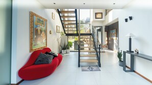 A modern living room with a red sofa, a staircase, and a large painting on the wall.