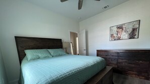 Een slaapkamer met een bed, een houten hoofdeinde, een bankje aan het voeteneinde van het bed, een dressoir en een deur naar een andere kamer.