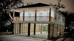 Een huis met twee verdiepingen, voorzien van een balkon op de bovenverdieping, dat rust op houten palen, en een overdekt terras met een houten hek.