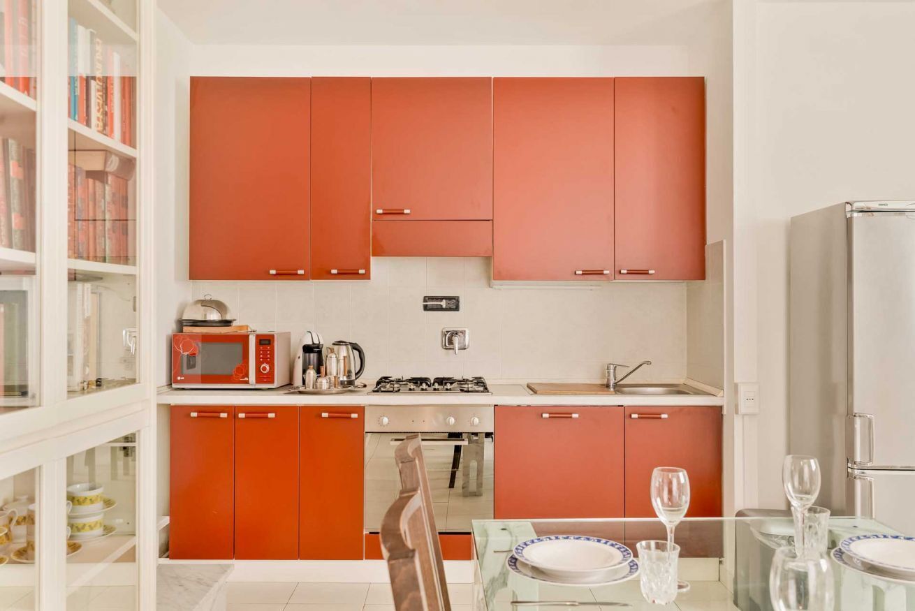 Une cuisine compacte avec des meubles de rangement rouges, un four à micro-ondes, une cuisinière et un coin repas comprenant une table et des chaises.
