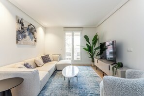 Ein modernes Wohnzimmer mit einer Couch, einem Couchtisch, einem Fernseher und einer großen Pflanze.