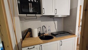 A compact kitchen with white cabinets, a black oven, a sink, and a wooden countertop. - Le case di reno (Lucoli)