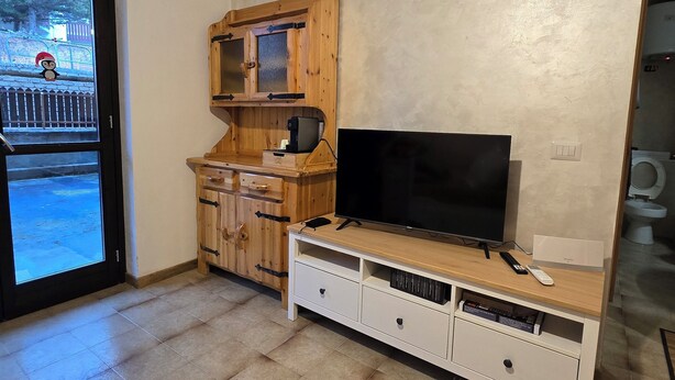 A room with a wooden cabinet, a flat-screen TV, and a sliding glass door leading to an outdoor area. - Le case di reno (Lucoli)