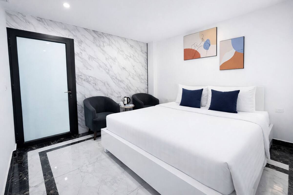 Een moderne hotelkamer met een groot bed, een zithoek met twee fauteuils, een salontafel en abstracte wanddecoratie.