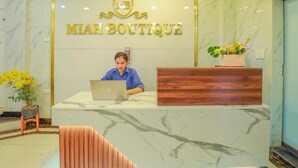 Un comptoir d'accueil avec une enseigne indiquant « MIAH BOUTIQUE » et une personne assise au comptoir, devant un ordinateur portable.