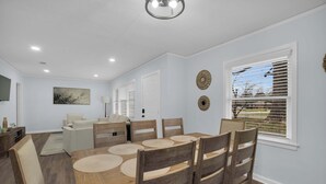Ein Essbereich mit Holztisch und Stühlen, einer Couch und einem Fernseher im Hintergrund.