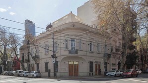 A historic building with a central archway, multiple balconies, and a row of parked cars along the street. - MOT Rentals + 4Bd with Terrace, Pool & BBQ in La Rural (Buenos Aires)