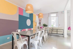 A dining area with a long table, white chairs, and wicker pendant lights. - MOT Rentals + 4Bd with Terrace, Pool & BBQ in La Rural (Buenos Aires)