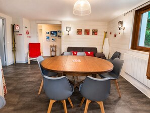 A dining area with a round wooden table surrounded by chairs, a red chair, and a ski rack in the corner. - Ground-floor apartment near the slopes in Les Rousses (Prémanon)