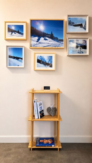 Una pared con seis fotografías enmarcadas que muestran paisajes nevados, una estantería de madera con libros y objetos decorativos, y una pequeña señal encima de la estantería.