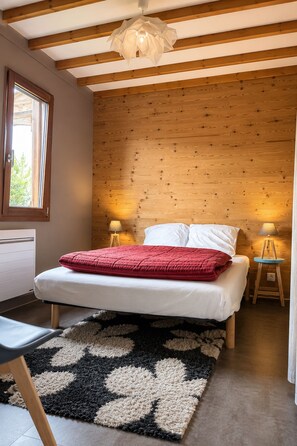 A bedroom with a bed, two bedside lamps, a window, and a wooden ceiling. - Top-floor apartment, chalet on the slopes of Les Rousses (Prémanon)