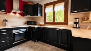 A modern kitchen with black cabinets, a stainless steel range hood, a microwave, and a coffee maker. - Upstairs apartment, chalet on the slopes of Les Rousses (Prémanon)