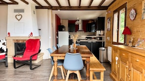 Un comedor con mesa y sillas de madera, una chimenea y una cocina al fondo.