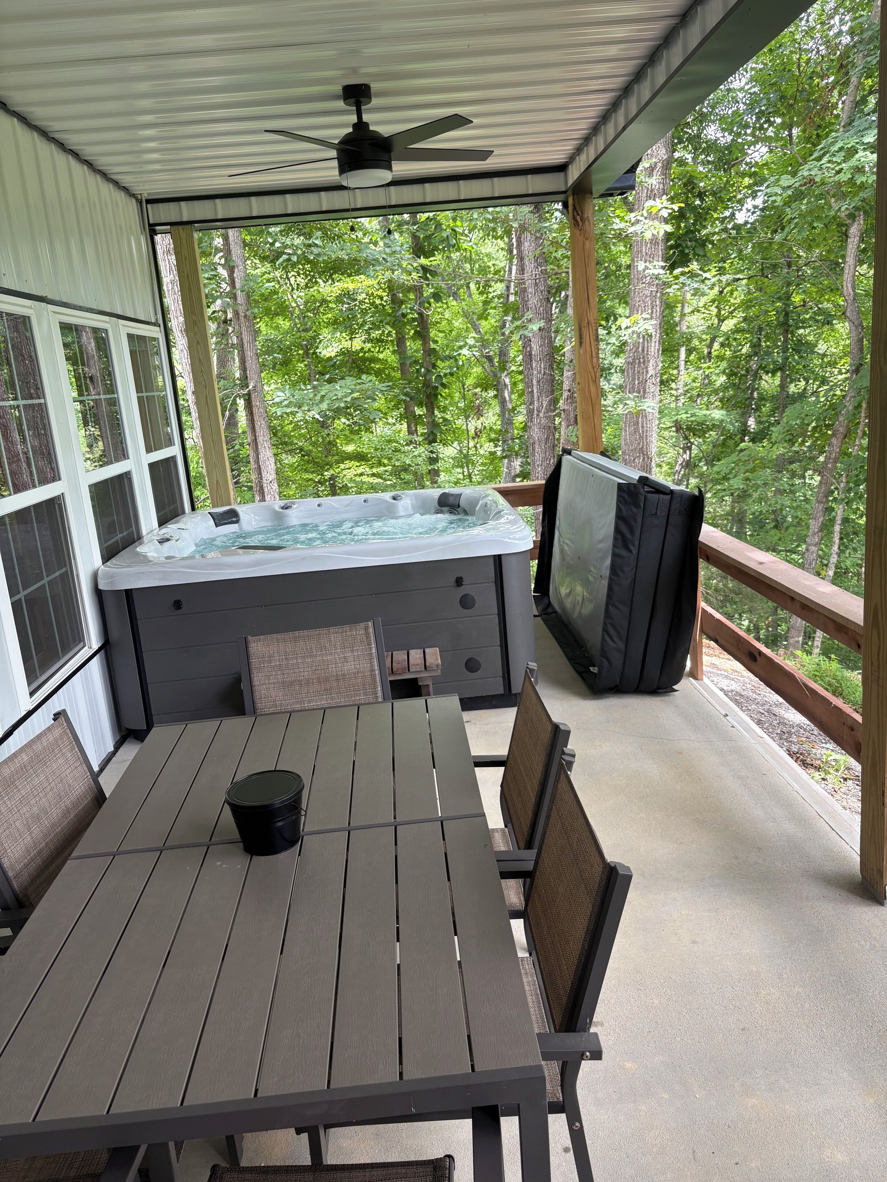 A covered outdoor area with a hot tub, seating, and a television.
