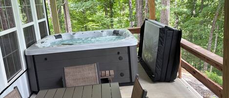 A covered outdoor area with a hot tub, seating, and a television.