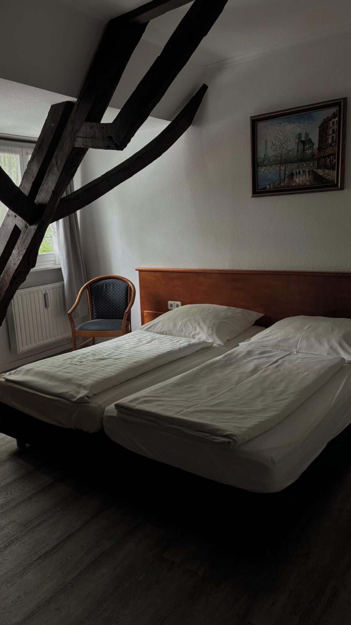 Una habitación con una cama, una silla, un cuadro y una ventana.