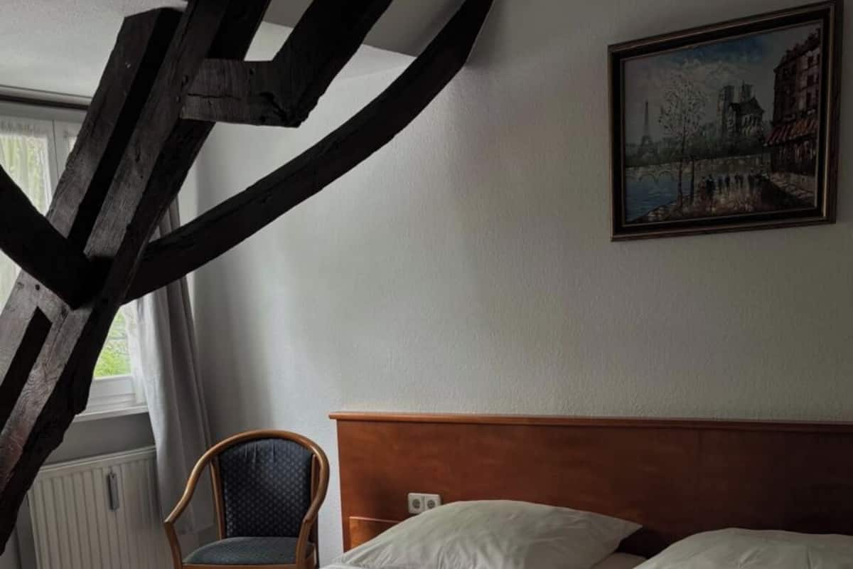 Une pièce avec un lit, une chaise, un tableau et une fenêtre.