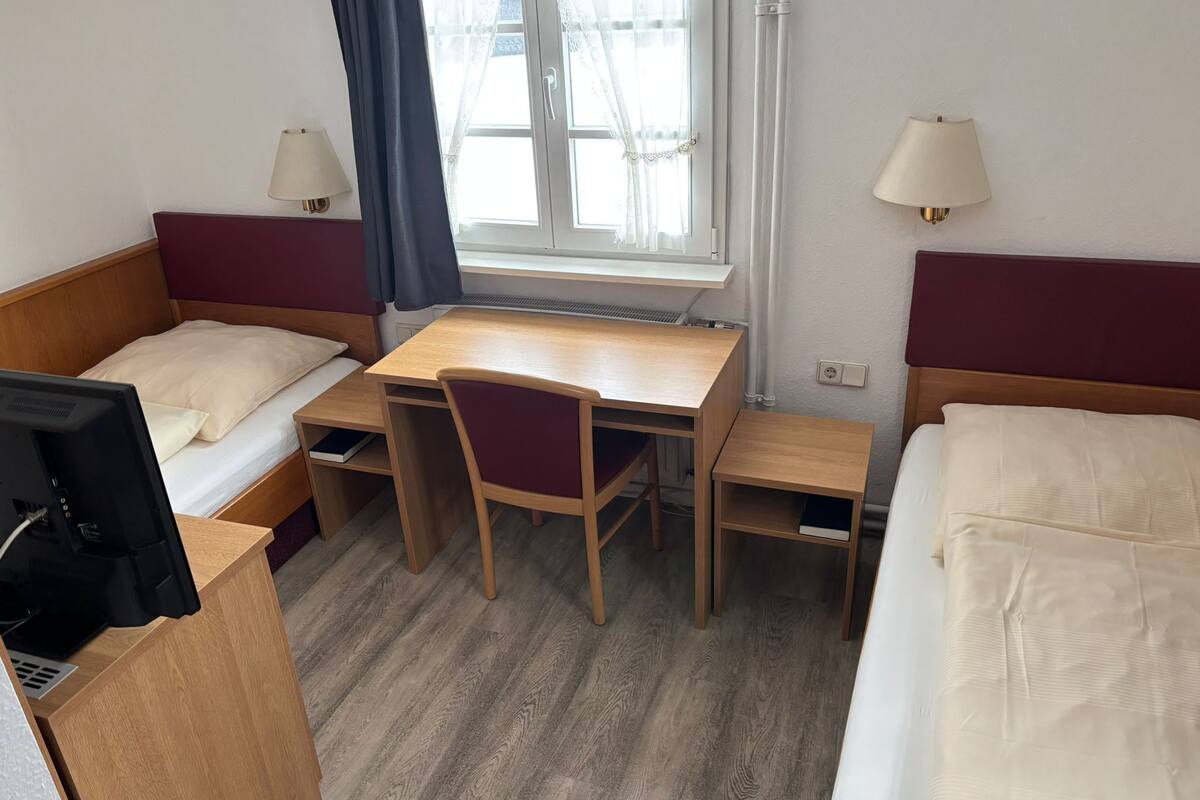 Une chambre d’hôtel avec deux lits simples, un bureau en bois, une chaise, une télévision et deux lampes de chevet.