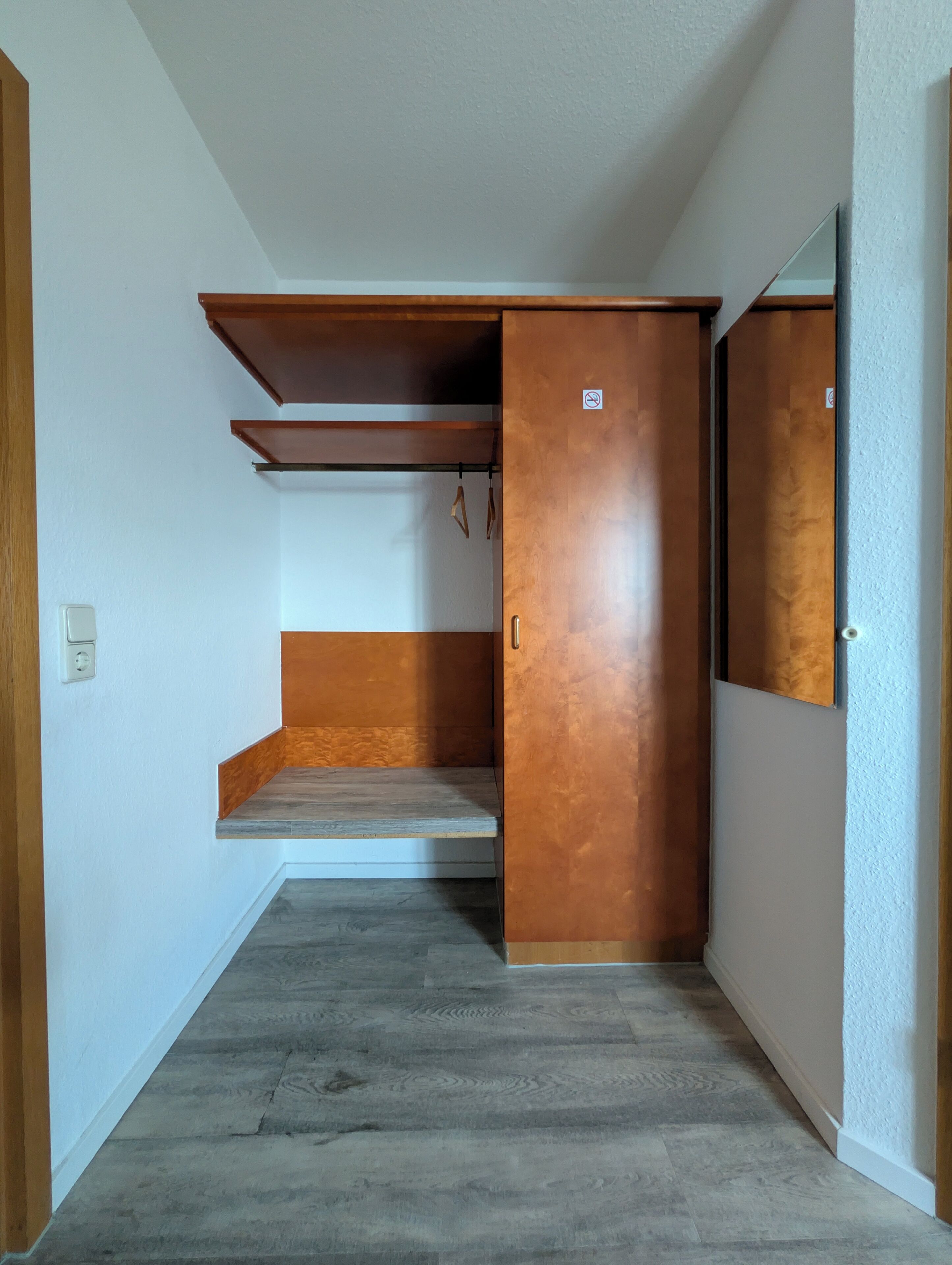 A room with a wooden wardrobe, a small shelf, and a mirror.
