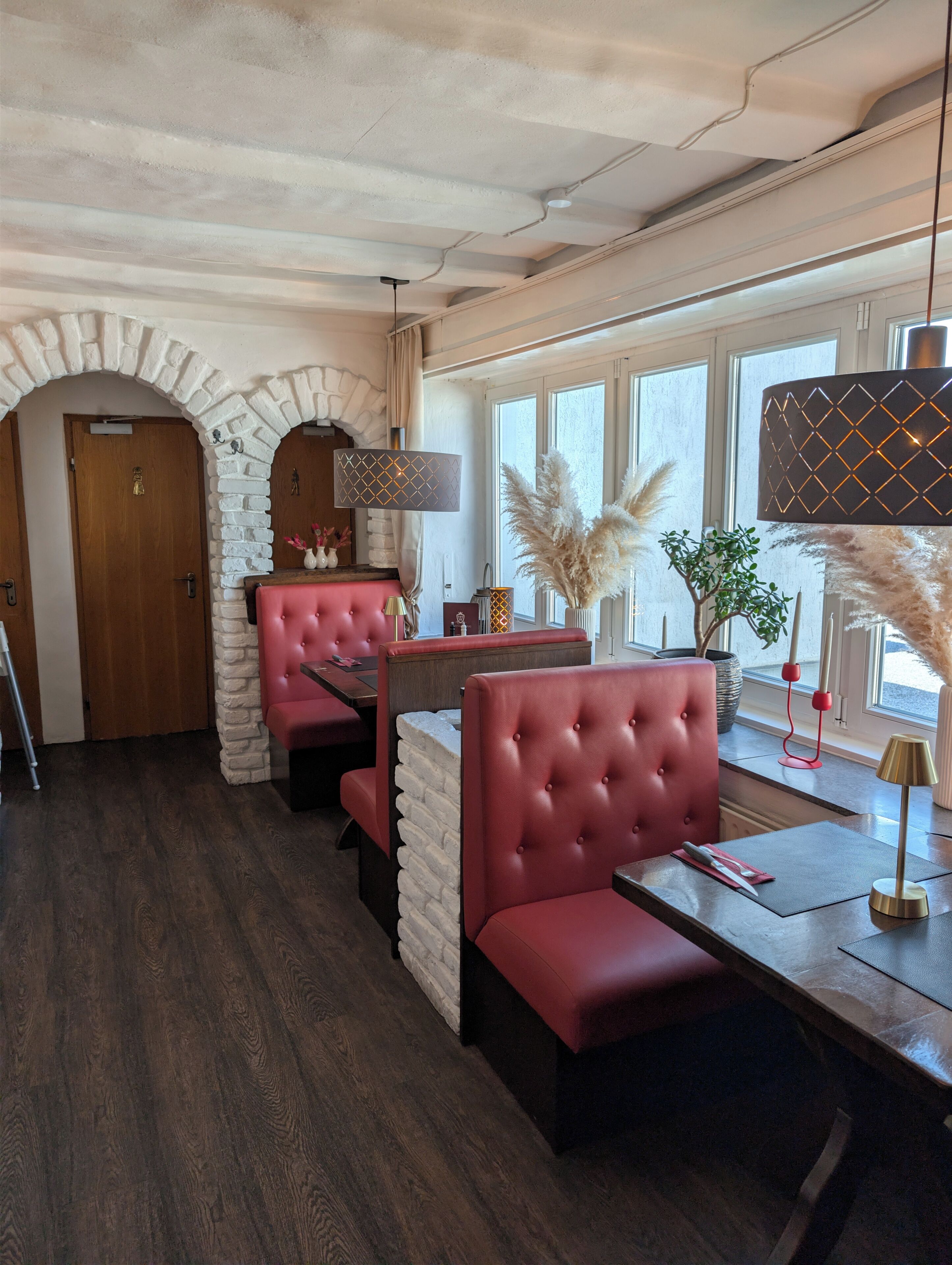 A restaurant interior with brick arches, red upholstered booths, and a wooden floor.