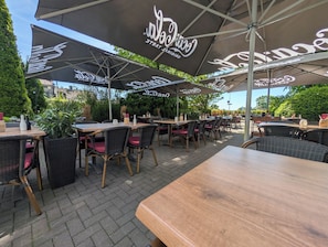 An outdoor café with tables and chairs under umbrellas, surrounded by greenery. - Westfalenkrug (Wuppertal)