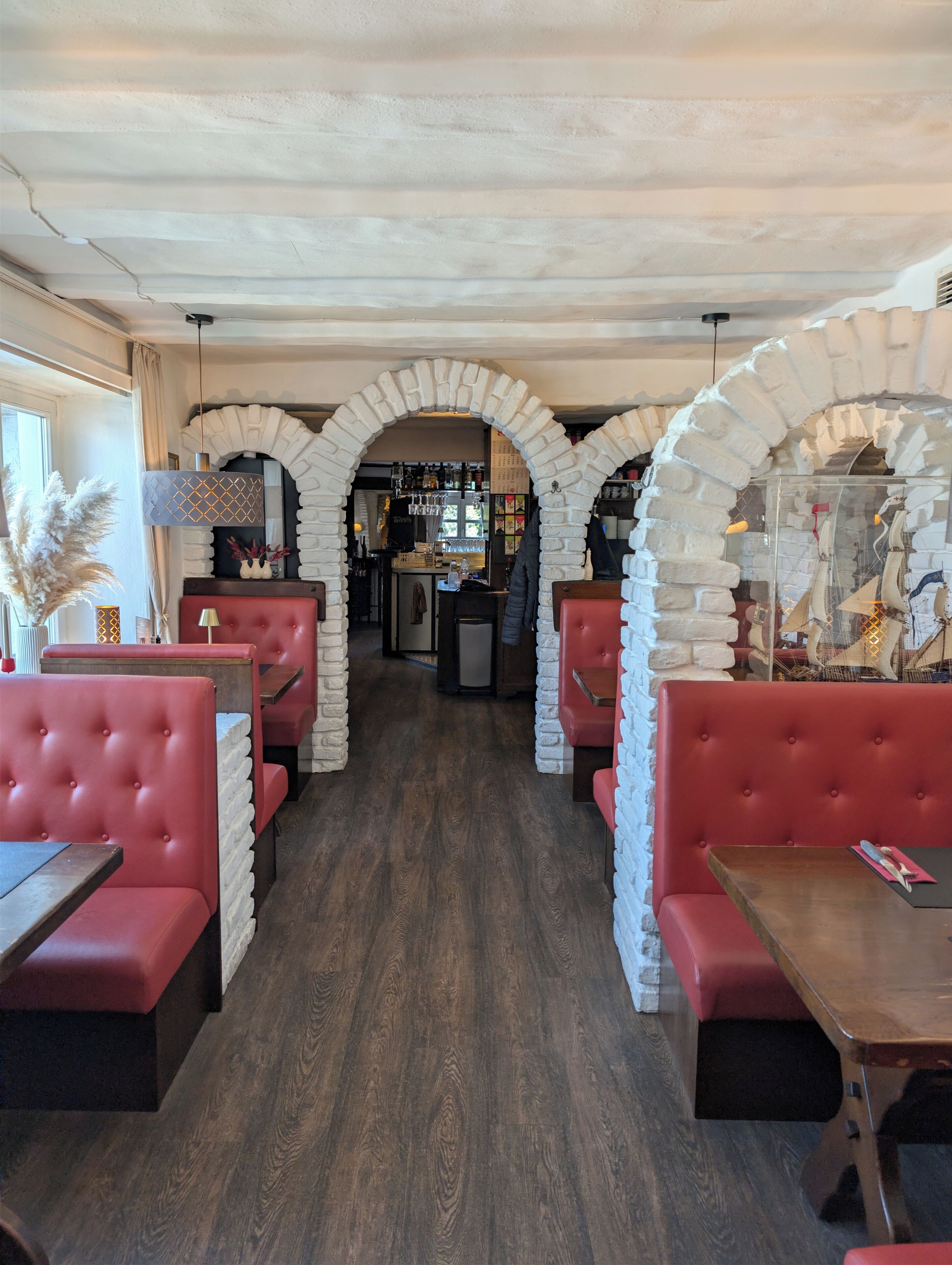 Ein Restaurant mit roten Sitzbänken, weißen Ziegelbögen und einer Bar im Hintergrund.